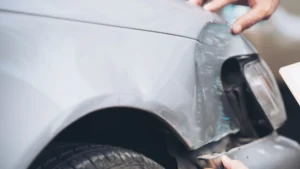 Perito revisando el daño en la aleta delantera de un coche gris durante un contraperitaje
