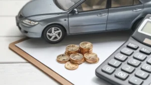 Maqueta de un coche, monedas y una calculadora sobre una carpeta, para calcular el impuesto de matriculación