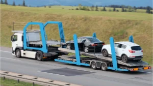 Camión portavehículos circulando por autovía con dos coches cargados en la plataforma superior