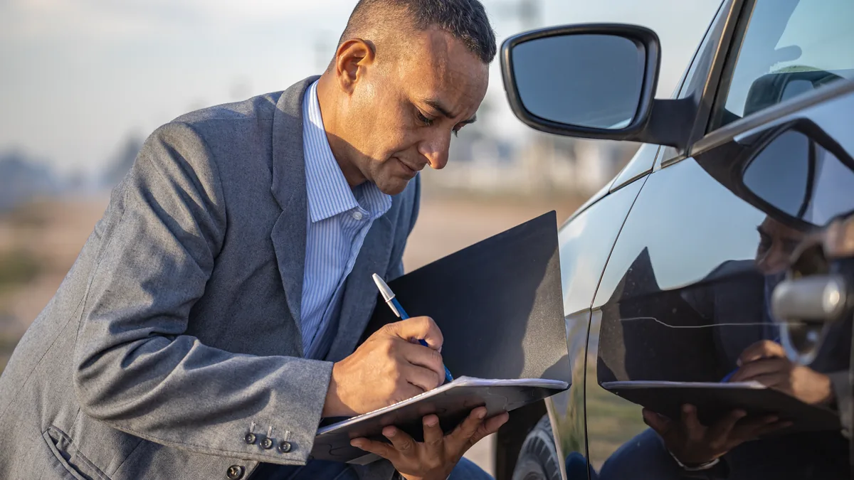 Perito de vehículos tomando notas junto a un coche durante una inspección